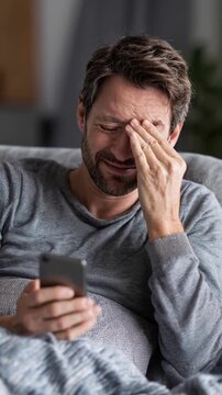 Tired man with eye strain using smartphone at home