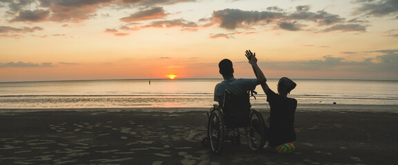 Cinematic scene of wheelchair user and caregiver watching beautiful sunset at the beach, concept of freedom, accessible tourism, inclusion and emotional family connection.