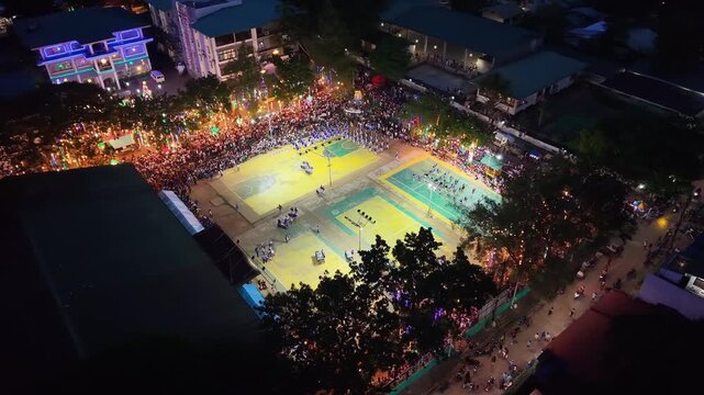 Night aerial view of a crowded outdoor drum performance on illuminated basketball courts in Coron with spectators gathered around the town venue