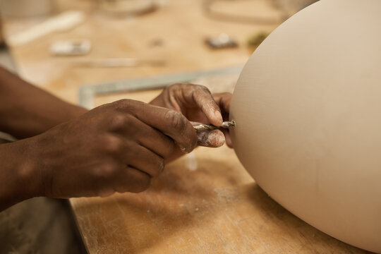 African ceramist making a hole in a pot using a drill bit at a bench