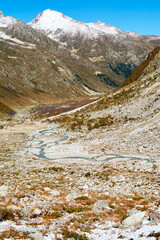 High-altitude river winds through yellow autumn valley where golden water mirrors seasonal mountain colors.