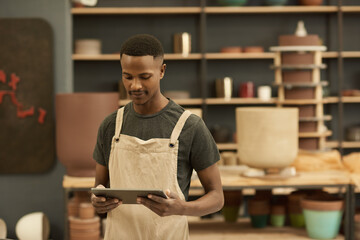 Young African potter using a tablet in a large ceramics workshop