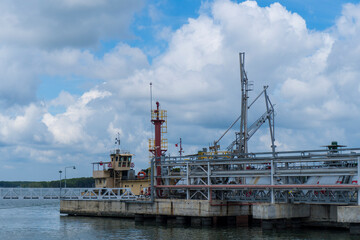 Large ship is docked at a pier with a red and white light on top. The sky is cloudy and the water is calm