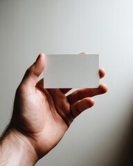 Obraz premium A hand holding a blank white business card between fingers. Concept Close-up hand, Blank business card, Minimalist, Fingers holding card, Card between fingers