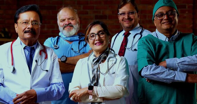 Indian confident doctors standing in group looking at camera portrait of senior surgeons and physicians with confident smiles wearing medical coats inside modern hospital healthcare ward