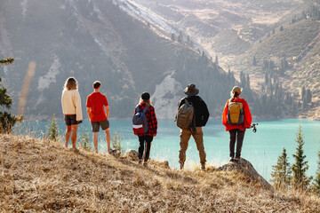 Group of hikers or tourists with backpacks are standing high in mountains and looks and enjoys view at mountain lake