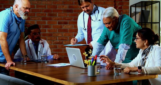 Indian confident doctors discussing case on laptop together senior surgeons and physicians reviewing digital medical records on desk in hospital while deciding proper course of action for treatment