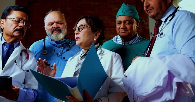 Indian confident doctors discussing case paper together senior surgeons and physicians reviewing patient chart file before operation while standing as medical team finding treatment solution