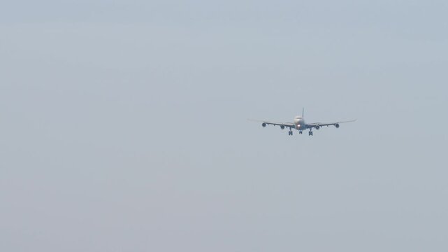 A huge four-engine aircraft with an unrecognizable livery approaching landing, front view long shot. Airplane in blue sky background. Travel concept