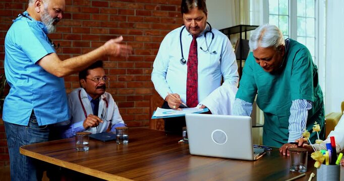Indian confident doctors discussing case on laptop together senior surgeons and physicians reviewing digital medical records on desk in hospital while deciding proper course of action for treatment