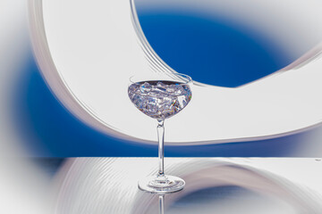 Close up view of elegant cocktail glass with ice cubes on abstract blue and white background.