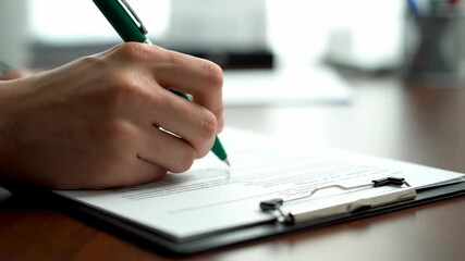 Signing Legal Documents - A person is shown signing a document on a clipboard using a green pen. The video focuses on the hand and pen as the signature is made on the legal agreement. - Powered by Adobe