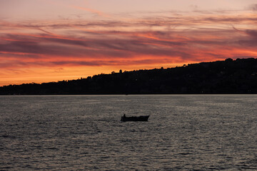 Naklejka premium Naples Italy fishing boat at sunset on the Bay of Naples red clouds over Posillipo hill calm sea silhouette evening seascape Mediterranean coast Campania travel tourism scenic view