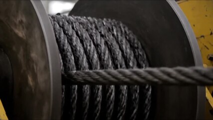 Close-up of a thick steel wire rope slowly winding onto a large industrial winch drum, showcasing the heavy-duty mechanical process in an industrial setting.