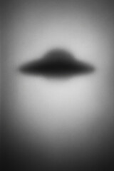 A blurred silhouette of a flying saucer against a soft, light background. The image evokes themes of extraterrestrial life and science fiction.