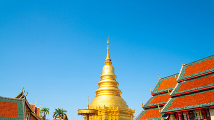 Majestic Golden Pagoda under Clear Blue Sky with Lush Green Trees, Traditional Thai Buddhist Architecture