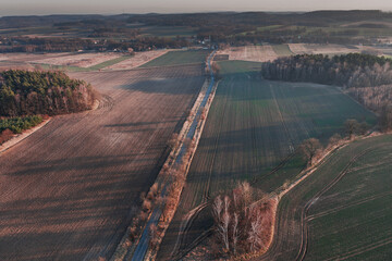 Droga przebiegająca przez r&oacute;wninę pokrytą polami uprawnymi, łąkami, kępami drzew. Jest słoneczny dzień. Zdjęcie wykonano z dużej wysokości z użyciem drona.