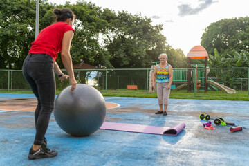 Personal trainer holding fitness ball for senior woman exercise outdoors
