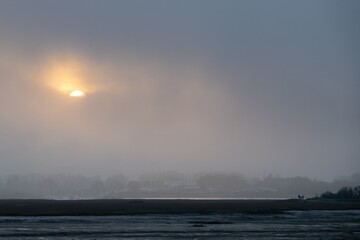 sun starting to set through the cloud on a winter day over the mud flaps at Emsworth Hampshire England
