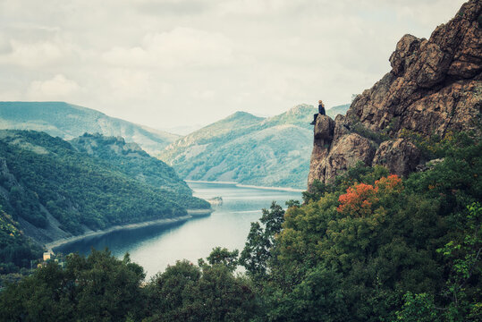 A woman on the top of a rock enjoys the view of an autumn forest and Studen Kladenec dam, Bulgaria