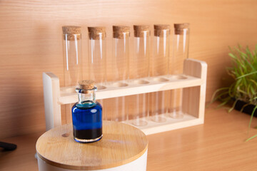 Test tubes on a wooden rack with a small bottle of blue liquid placed on a table in a laboratory setting