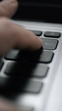 A finger pressing a Backspace key on a silver laptop keyboard. Vertical video.