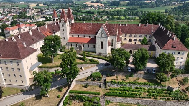 Aerial summer scenery of Sankt Paul im Lavanttal with monastery complex, rooftops, valley landscape, green hills, calm cinematic drone movement, warm atmospheric tones
