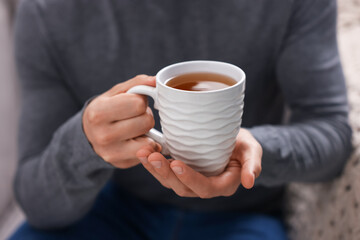 Man with cup of hot tea indoors, closeup