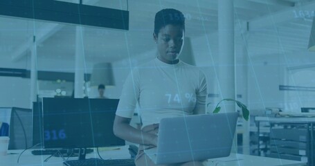 Typing woman in light top on laptop in open office, showing data overlay and coffee cup