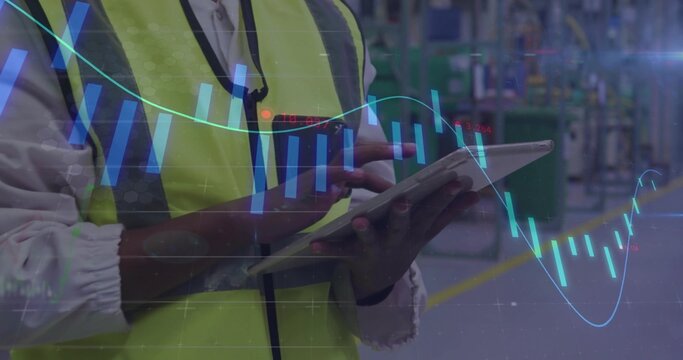 Holding female technician in high-vis vest tapping tablet on factory floor, with candlestick charts - Powered by Adobe