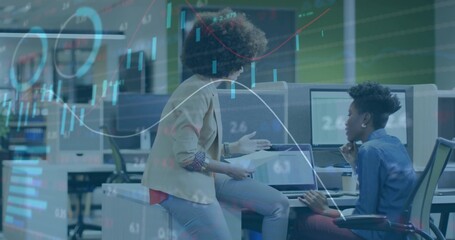 Reviewing coworkers analyzing charts at open office, monitors papers chart overlays business-casual
