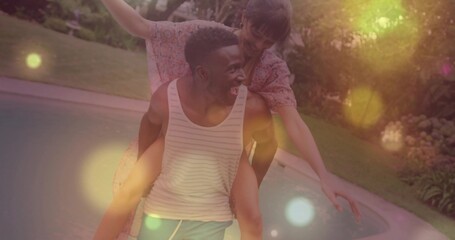 Carrying man giving woman piggyback at backyard pool, wearing striped tank top and floral dress