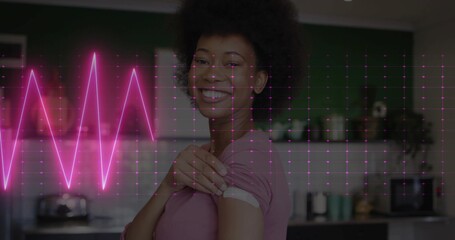 Smiling woman pulling up sleeve revealing bandage in kitchen in pink shirt with neon EKG overlay