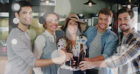 Clinking five adults cheering and toasting at bar counter, with dark bottles and wide-brim hat