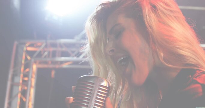Singing female performer gripping vintage mic grille on performance stage, in dark jacket