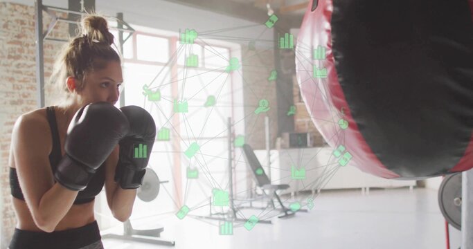 Punching gloved boxer wearing black sports bra, facing heavy bag in gym, data overlay, copy space - Powered by Adobe