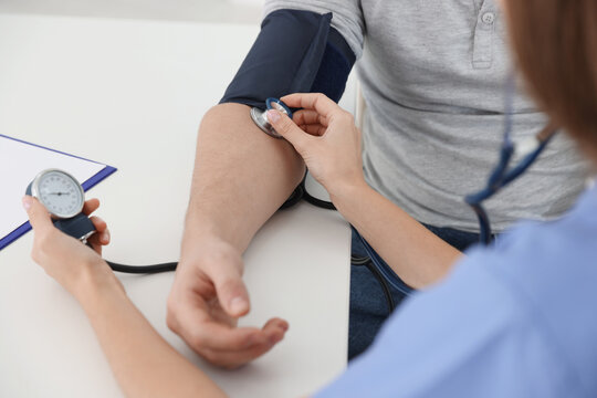 Nurse checking man's blood pressure with sphygmomanometer at table in hospital, closeup