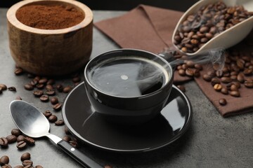 Aromatic coffee in cup and beans on grey table, closeup