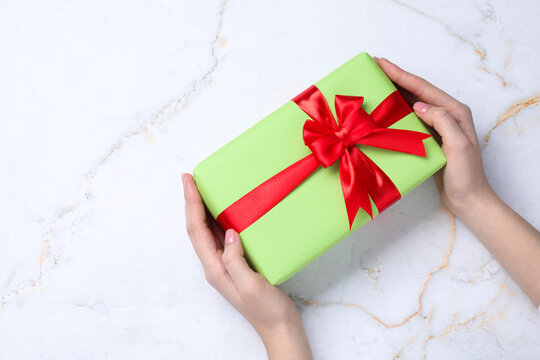 Woman with beautiful wrapped gift on white marble background, top view. Space for text