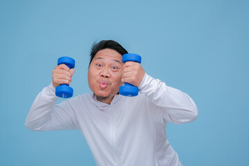Close up of young Asian man in the gym lifting dumbbell wearing white t-shirt with happy laughing expression on turquoise blue background