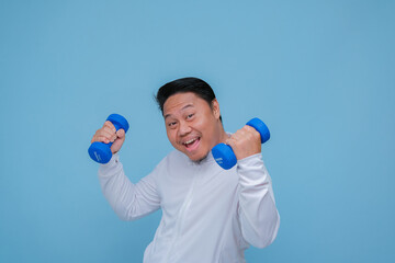 Close up of young Asian man in the gym lifting dumbbell wearing white t-shirt with happy laughing expression on turquoise blue background