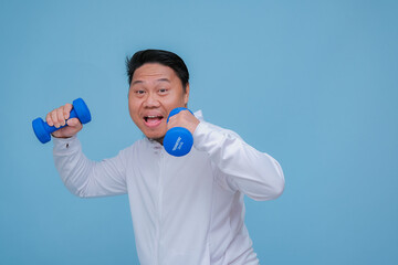 Close up of young Asian man in the gym lifting dumbbell wearing white t-shirt with happy laughing expression on turquoise blue background