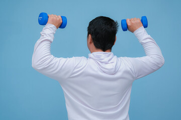 young asian man lifting dumbbells in both hands, seen from behind wearing a white t-shirt on turquoise blue background 