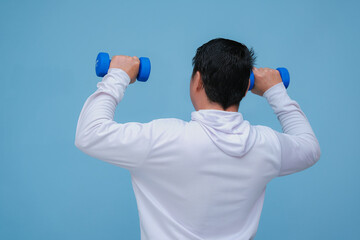 young asian man lifting dumbbells in both hands, seen from behind wearing a white t-shirt on turquoise blue background 