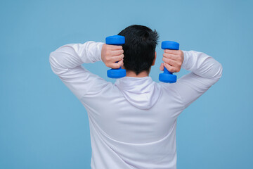 young asian man lifting dumbbells in both hands, seen from behind wearing a white t-shirt on turquoise blue background 