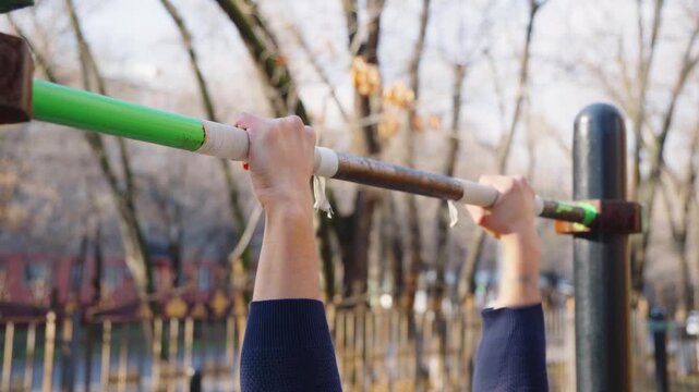 Close up of hands on a pull-up bar outdoors.