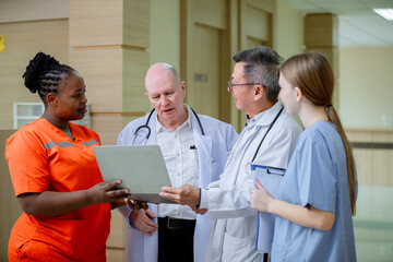 diverse team of medical professionals stands in a bright hospital corridor, reviewing information on a laptop. The group includes doctors and nurses wearing different colored uniforms, 