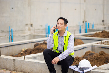 Mobile Phone. building and construction worker using mobile phone, Asian male wearing safety hard hat helmet working at construction site. Professional Architects Engineer,  Civil Engineering
