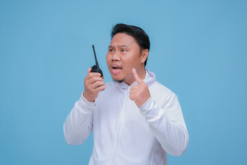 Young Asian man talking on Handy Talkie with very angry expression wearing white t-shirt on turquoise blue backgroun