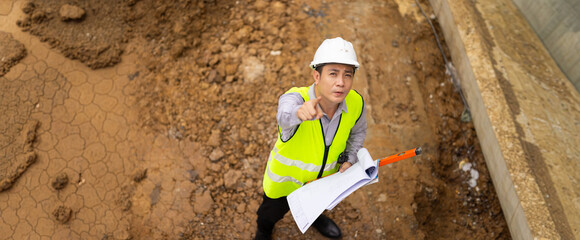 Portrait Professional Architects Engineer at construction site. Asian Man working, Architect or contractor working on house building under construction site. Civil Engineering in safety harthat helmet